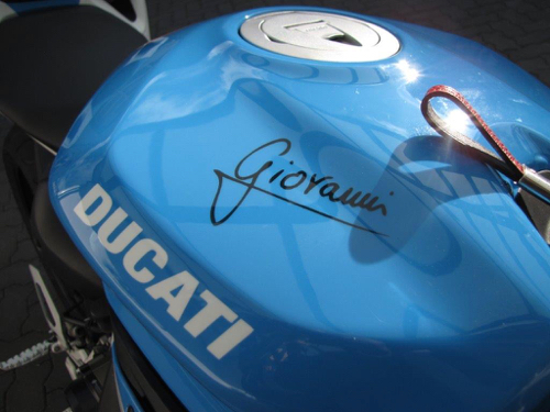 Nahaufnahme des Stauraums eines blau-weißen Motorrads mit der Unterschrift von Giovanni und einem Ducati Schriftzug