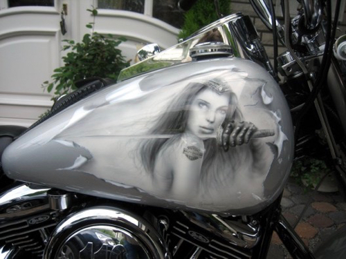 Nahaufnahme eines silbernen Seitenteils eines Motorrads mit einem Airbrush-Bild einer Frau mit langen Haaren, die ein Schwert vor sich hält