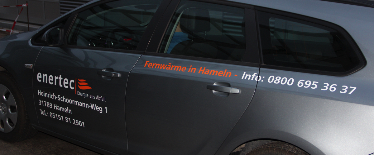 Beschriftung 'enertec Energie aus Abfall' auf der vorderen linken Tür eines silbernen Autos